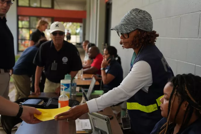 Photo of someone handing a yellow piece of paper to someone else